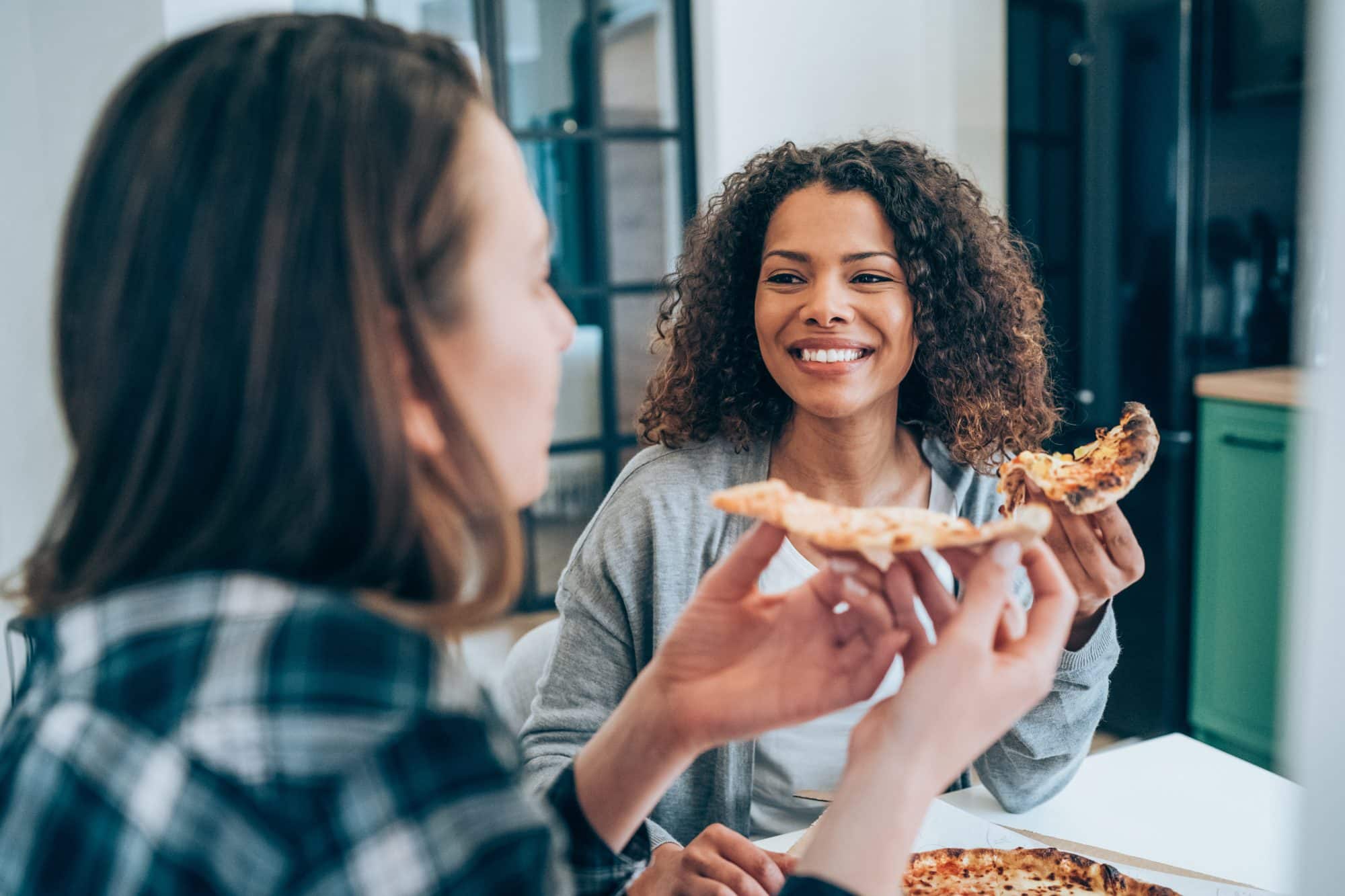 two young women eating pizza together at home.